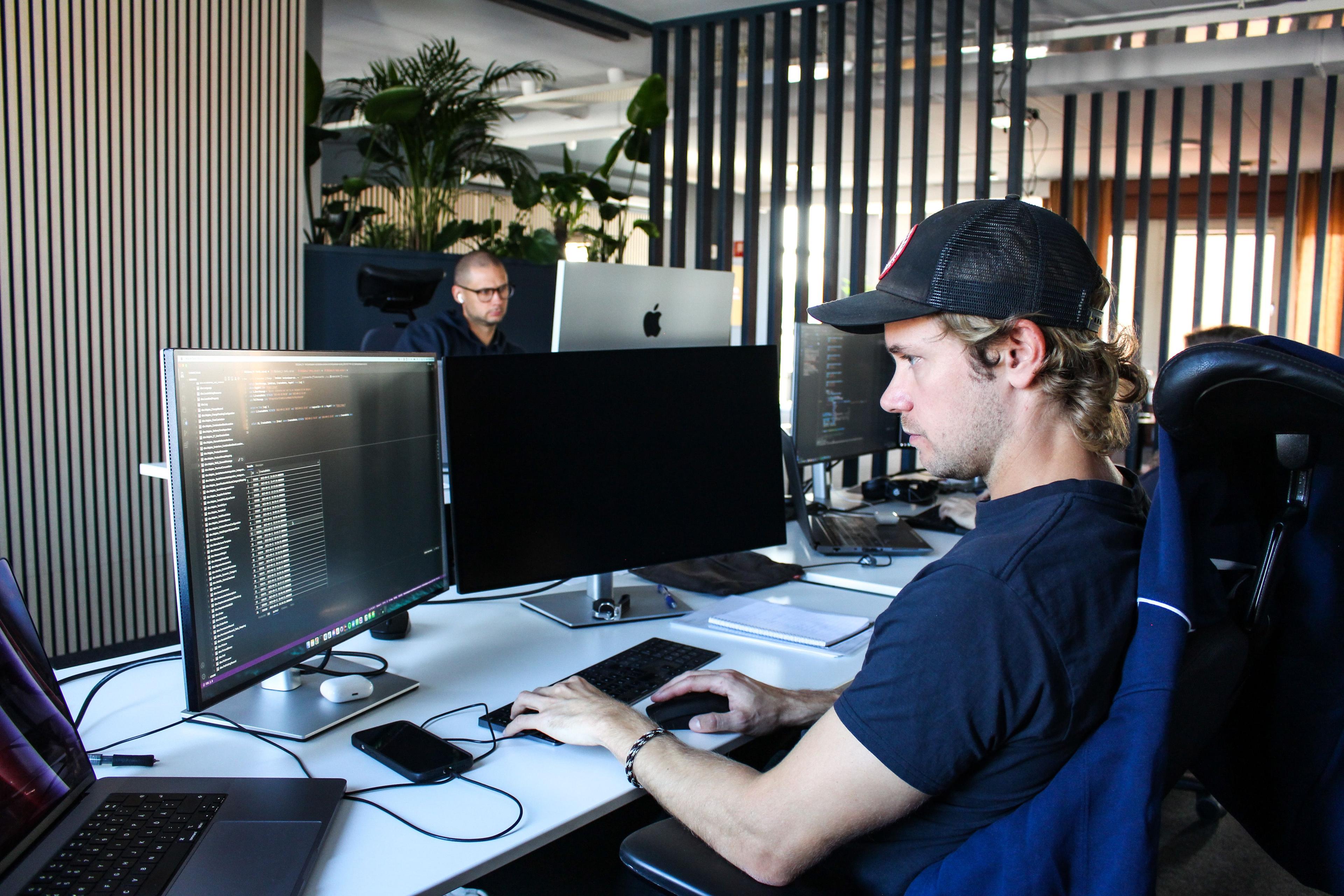 En man arbetar vid sitt skrivbord där datorskärmar med kodtext står.