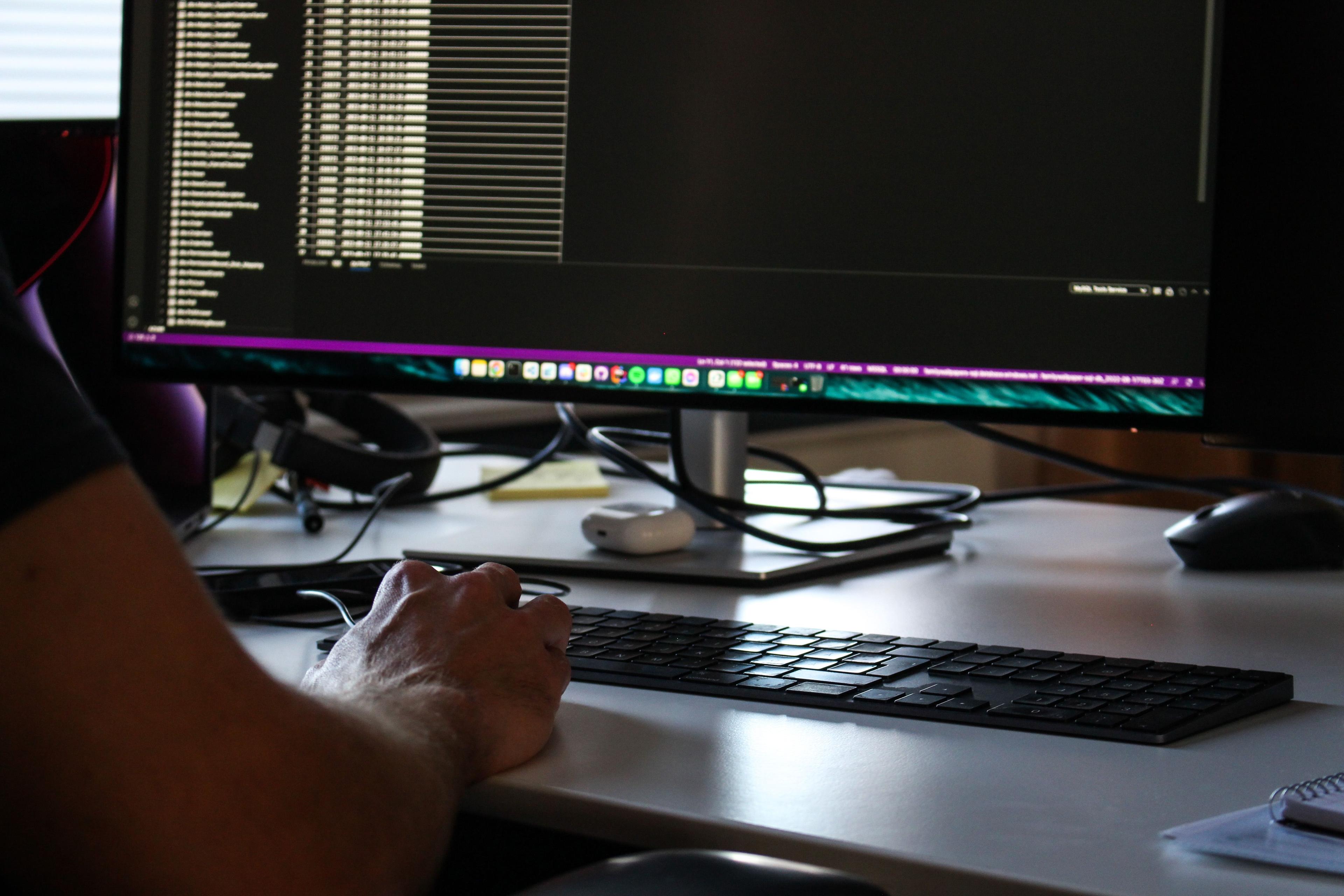 Datorskärm med kodtext, en arm i förgrunden.